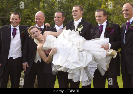 Young bride being lifted by the groom, best man and ushers. Stock Photo