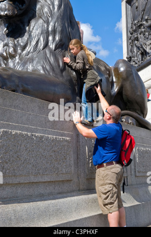 London , Westminster , Trafalgar Square , father gives helping hand to pretty young daughter climbing lion at Nelsons Column Stock Photo