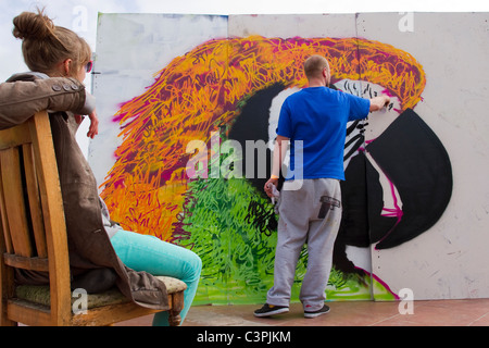 Ives St. Covert with assistant sat on a bench. Graffiti Artist at work at the Southport Jam Legal Wall  UpNorthFest Merseyside, UK Stock Photo