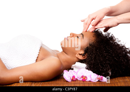 Brazilian woman at day spa, laying on bamboo massage table with head on pillow wearing a towel getting a facial massage. Stock Photo