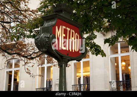 An iconic Parisian Art Nouveau Métro sign. In the background can be seen the elegant windows of an upmarket shop in the Champs Elysées. Paris, France. Stock Photo