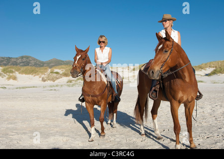 2 people riding horses on the beach Stock Photo