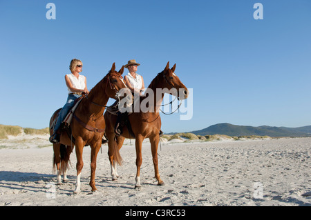 2 people riding horses on the beach Stock Photo