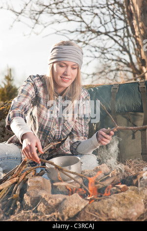 Young hiking woman with backpack cook on campfire in countryside Stock Photo