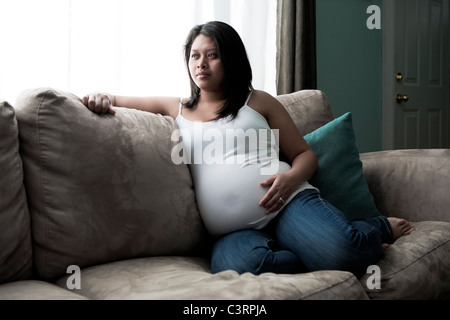 Expectant Mother sitting on couch in front of window Stock Photo