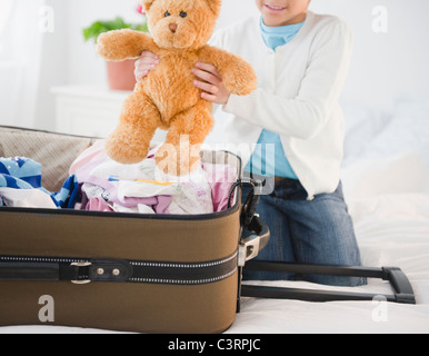 African American girl putting teddy bear in suitcase