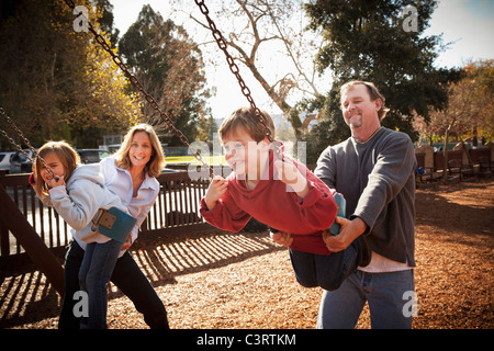 Caucasian parents swinging children on swing set Stock Photo