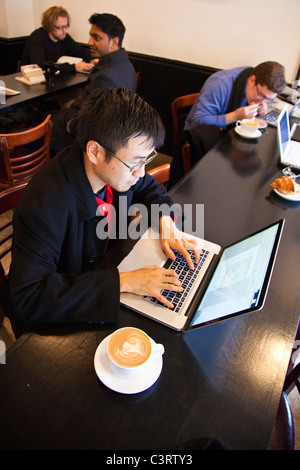 Korean American typing on an Apple laptop and drinking a cappuccino at 9th street espresso, Manhattan, New York City Stock Photo