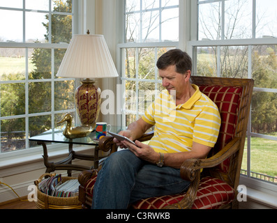 Senior man sitting at home reading on his iPad Stock Photo