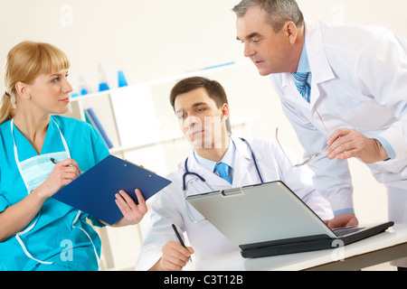 Photo of aged physician and young clinician looking at document in nurse’s hand Stock Photo