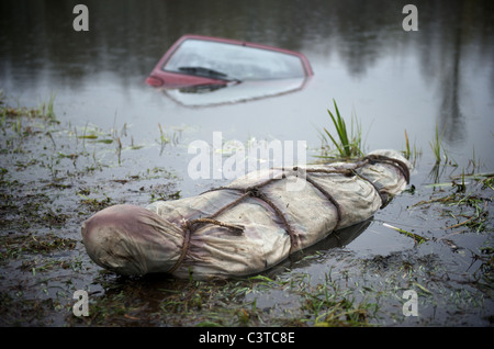 A car half-sunken in a lake with a body bag in the foreground Stock Photo