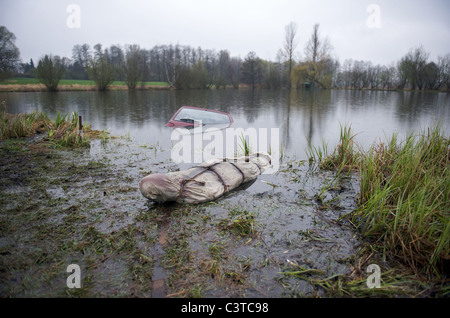 A car half-sunken in a lake with a body bag in the foreground Stock Photo