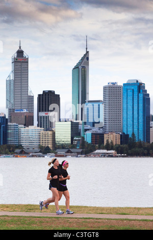 Two women jogging on path beside river with city in the background. Stock Photo