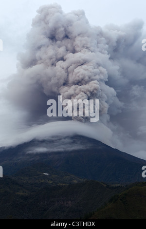 A powerful volcanic eruption is captured as a massive, dense plume of gray and white ash and steam billows upward from the summit of a mountain. The eruption column rises high into the overcast sky Stock Photo