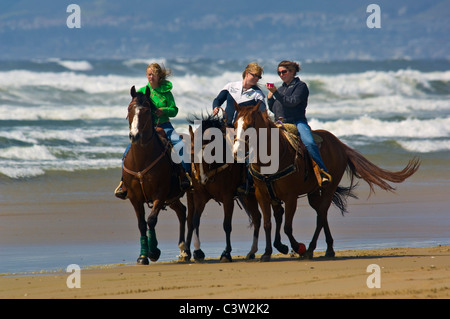 Three young women riding horses on the sand at Oceano State Beach, Oceano, California Stock Photo