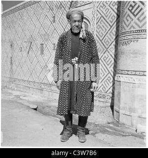 A portrait from the 1950s, of an elderly uzbek wearing traditional checked robe standing outside The Shir-Dar Madra,Uzbekistan. Stock Photo