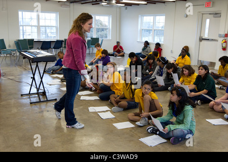 Middle school students look at sheet music before rehearsing song during music class taught by Anglo female teacher. Stock Photo