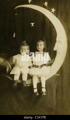 Circa 1910 photograph of a young boy and girl sitting on a paper moon. Studio photograph. Stock Photo