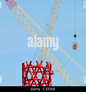 Construction cranes crisscross central red structural steel core ArcelorMittal Orbit tower two workers mid air in access cage London 2012 Olympics UK Stock Photo