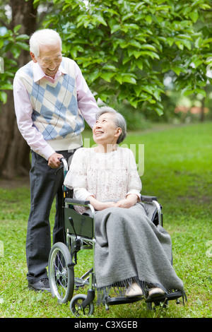 Senior man pushing senior woman on wheelchair, Tokyo Prefecture, Honshu, Japan Stock Photo