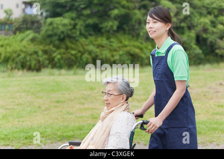 Healthcare worker pushing senior woman in wheelchair, Tokyo Prefecture, Honshu, Japan Stock Photo