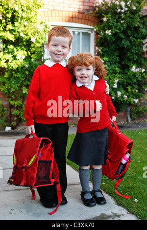 A 4 year old girl with ginger hair on her first day of school, with 6 year old brother. Both in school uniforms. Stock Photo