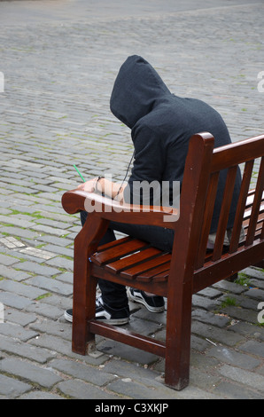 A youth wearing a hoodie sits on a bench in Parliament Square, Edinburgh. Stock Photo