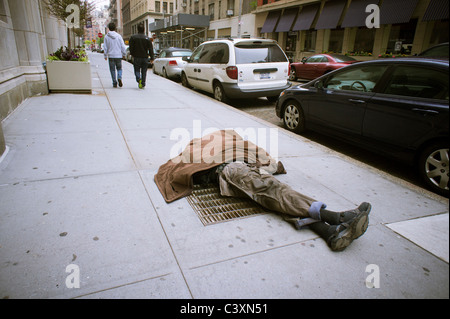 Homeless man sleeping on a vent in the sidewalk in Greenwich Village in New York Stock Photo