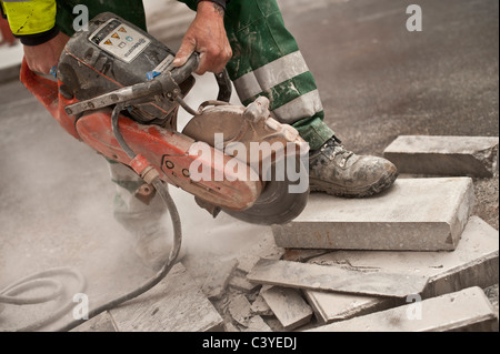 Dirty noisy dusty work; a man using an angle grinder to cut a paving stone, UK Stock Photo