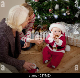 A baby dressed as Santa eating a biscuit Stock Photo