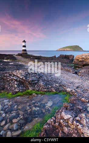 Twilight on the rocky Anglesey coast looking towards Penmon Point Lighthouse and Puffin Island, Anglesey, North Wales Stock Photo