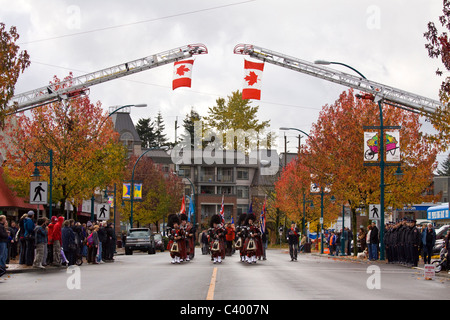Pipe band marches under flags suspend from fire ladders, 2009 Remembrance Day Parade, Port Coquitlam, BC, Canada Stock Photo