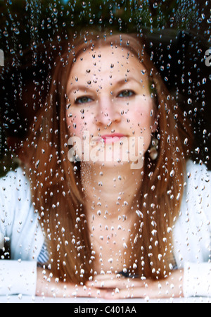 Girl looking through rain soaked window Stock Photo