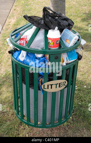 An overflowing litter bin on a post in a public park, Woolwich, East London, UK. Stock Photo