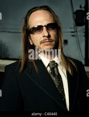 Close-up image of a scruffy, long-haired, balding man in sunglasses wearing a retro style suit. Stock Photo