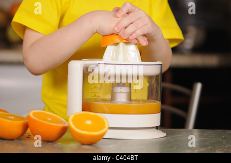 The child in a yellow vest to wring out juice from an orange Stock Photo