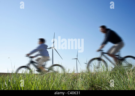 Father and son cycling past a windfarm Stock Photo