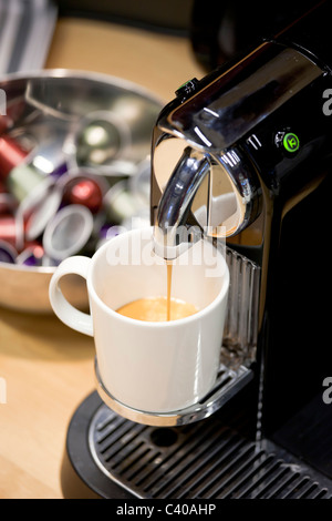 close up of Nespresso Coffee machine brewing freshly new espresso. Coffee capsules in a bowl in background Stock Photo