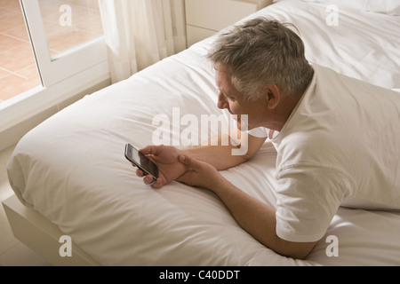 Mature man on bed using smart phone Stock Photo