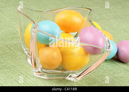 Close-up of some hard sugar coated chocolate eggs in a glass bowl, over a green background. Stock Photo
