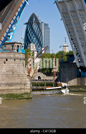 Sailing boat passing under grade 1 listed open Tower Bridge with the Gherkin in background London England Europe Stock Photo