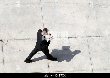 A young man in business attire walking while using a cell phone Stock Photo