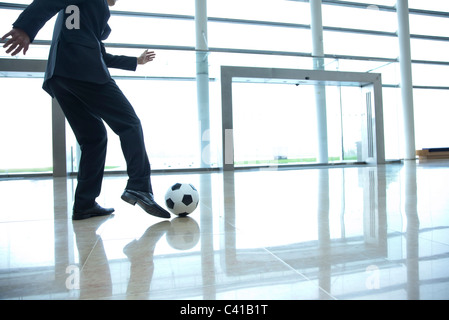 Businessman kicking soccer ball in lobby Stock Photo