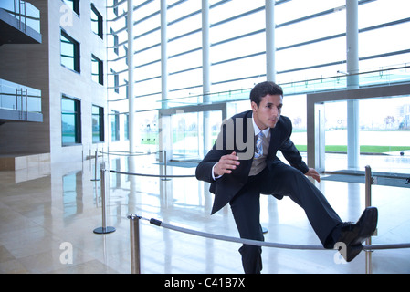 Businessman jumping over rope in lobby Stock Photo