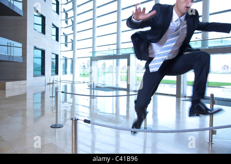 Businessman jumping over ropes in lobby Stock Photo