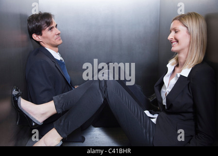 Colleagues trapped in elevator, sitting on floor chatting Stock Photo