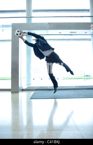 Businessman catching soccer ball in lobby Stock Photo