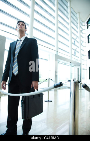 Businessman standing in lobby, looking up Stock Photo