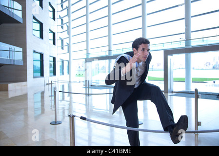 Businessman jumping over rope in lobby Stock Photo