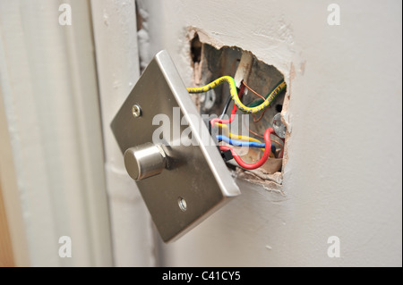 a faulty house light dimmer switch pulled away from wall showing electrical wires in parallel during DIY Stock Photo